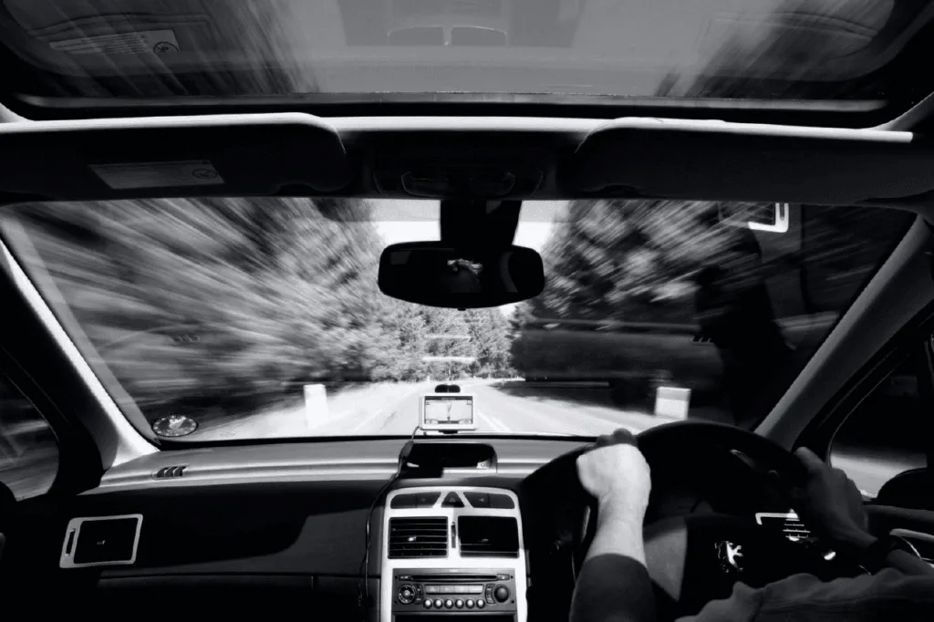 Black-and-white driver's-eye view from inside a car, looking through the windshield onto the road